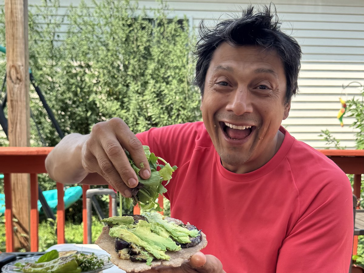 Jose laughing on a deck while holding a homemade avocado and eggplant tostada