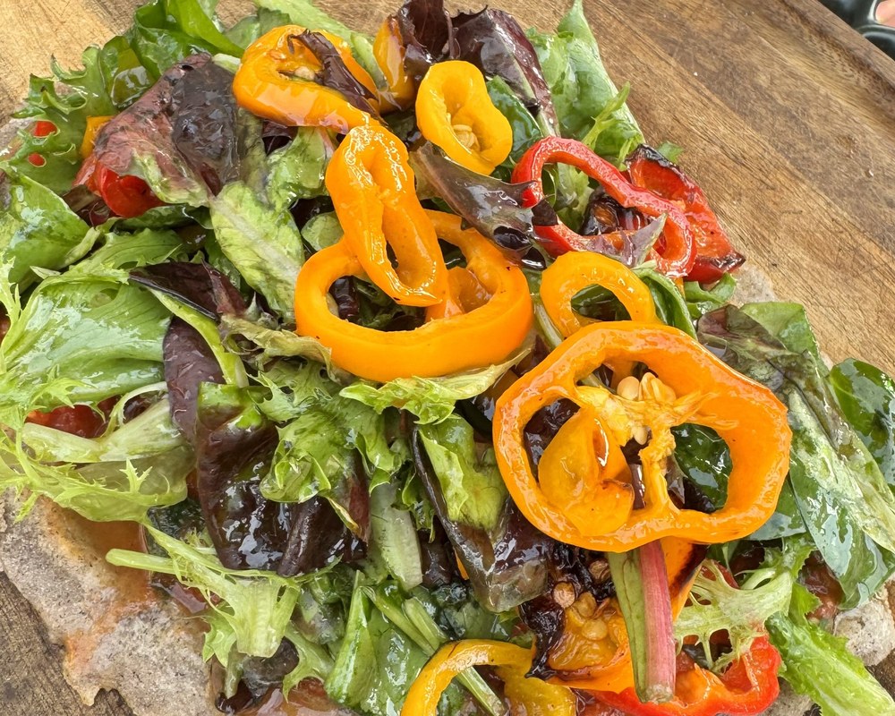 Crisp flatbread topped with mixed greens and roasted sweet peppers